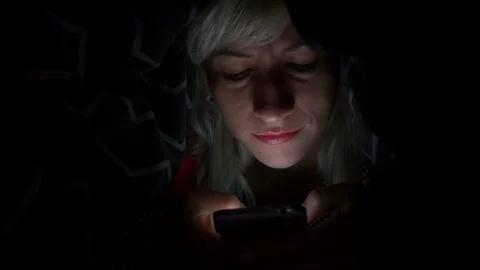 Joyful young woman using smart phone under the blanket in bed and smiling Stock Footage 72523375
