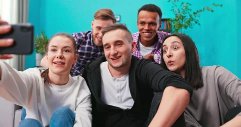 Joyous multi-ethnic group of friends sitting on couch together and taking selfie Vidéo 152368459