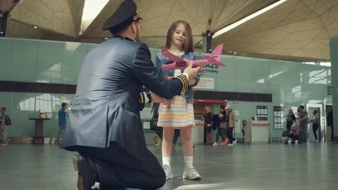 Joyous smiling pilot presenting toy pink plane to a little cute girl in terminal Stock Footage 108868544