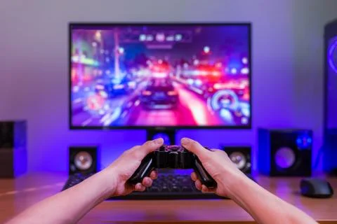 Joypad in hands. Computer gaming concept. Computer display with game in backg Stock Photos