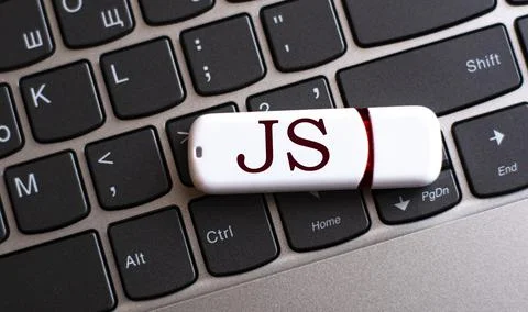 JS - the word on a white flash drive, lying on a black laptop keyboard Stock Photos