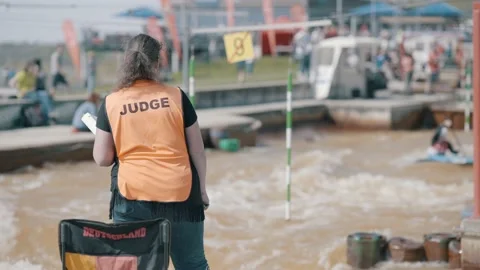 Judge in an orange vest making hand signs at a rafting championship on sunny day Stock Footage 239669344