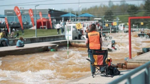 Judge in an orange vest making hand signs at a rafting championship on sunny day Stock Footage 239669358