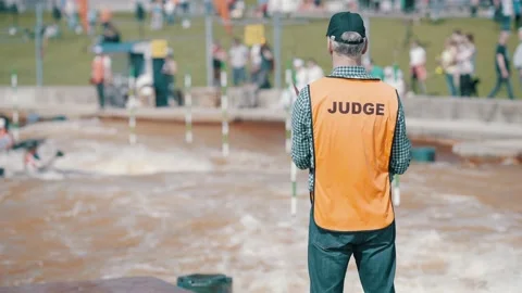 Judge in an orange vest making hand signs at a rafting championship on sunny day Stock Footage 239669383