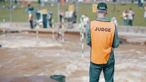 Judge in an orange vest making hand signs at a rafting championship on sunny day Stock Footage 239669398