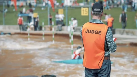 Judge in an orange vest making hand signs at a rafting championship on sunny day Stock Footage 239669424