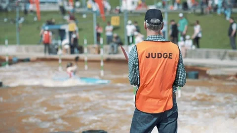 Judge in an orange vest making hand signs at a rafting championship on sunny day Stock Footage 239669430