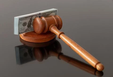 A judge's gavel placed beside a stack of dollar bills, creating a visual repr Stock Photos