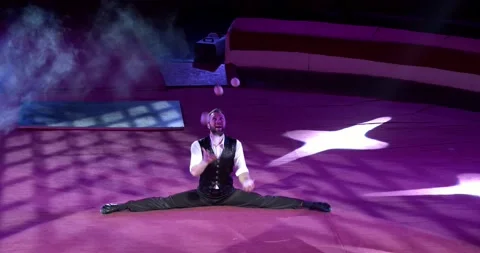 Juggler is doing a split while juggling five white balls on stage of a circus 4k Stock Footage 147486109