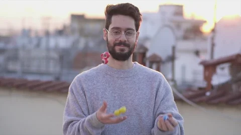 Juggler, Young Man Juggling with three funny eyes toys on a rooftop sunset ti Stock Footage 106724196