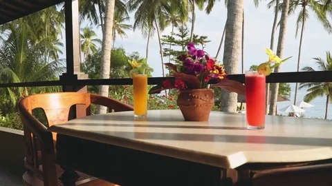 Juice and flowers on table on balcony in front of ocean and palm trees Stock Footage 77825360