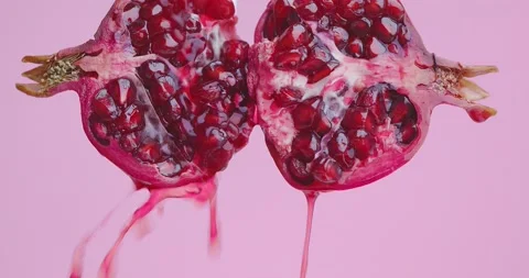 Juice flows down on halfs of natural red pomegranate fruit on pink studio Video stock 153058242