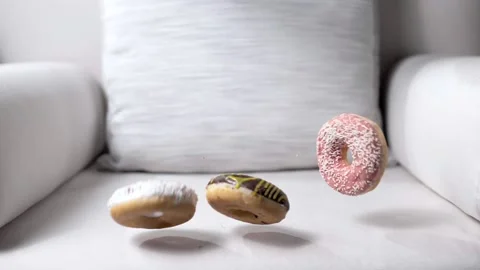 Juicy baked goods in colored icing fly and fall on the clean chair Stock Footage 191001331