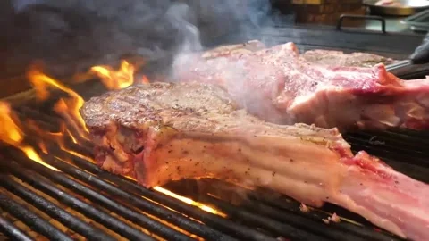 Juicy Barbecue Grilled Tomahawk Steak Sizzling on Charcoal BBQ Grill with Smoky Stock Footage 338213121