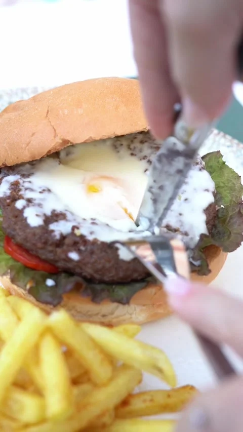 Juicy beef burger topped with fried egg, sauce, and fresh greens, close up 库存影片 334840431