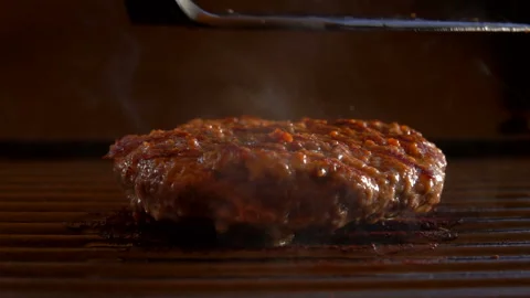 Juicy beef cutlet for a burger is pressed to the grill and burst into flames Stock Footage 129117796