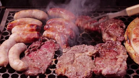 A juicy beef steak being pierced by a long fork on the grill alongside saus.. Vídeo Stock 337941084