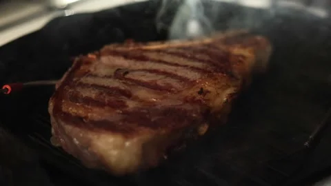 Juicy beef steak searing on a hot grill pan with visible smoke Stock Footage 340563244