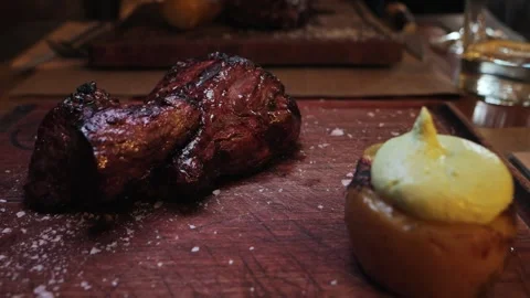 Juicy beef steak on a wooden surface with baked potatoes from the oven served Stock Footage 314109441