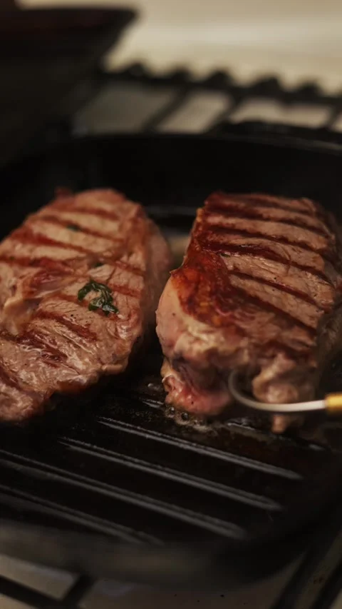 Juicy beef steaks sizzling on a cast iron grill pan with herbs Vidéo 340563389