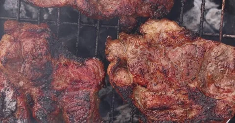 Juicy beef steaks sizzling on a hot grill with smoke rising Stock Footage 339069892