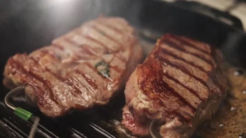 Juicy beef steaks sizzling on a hot grill with visible grill marks and steam Stock Footage 340563359