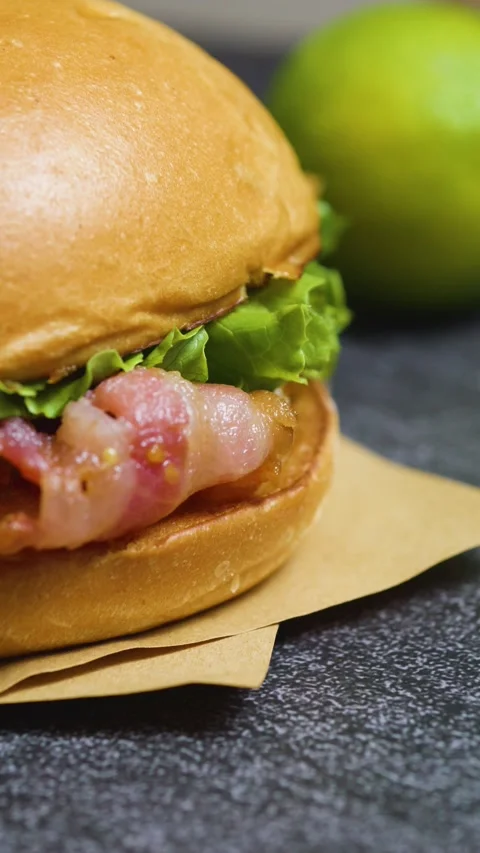 Juicy burger featuring crispy bacon and fresh lettuce, sitting on brown paper Stock Footage 314089975
