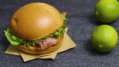 Juicy burger layered with crispy bacon, fresh lettuce resting on brown paper, Stock Footage 313165255
