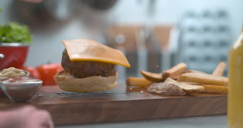 Juicy cheeseburger and fries falling onto a wooden board on a table with bright Stock Footage 199459348