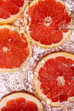 Juicy citrus fruit pattern with ruby red grapefruit slices under splashing .. Stock Photos