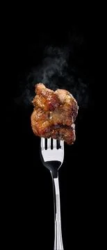 Juicy fried chicken piece on a fork with steam rising in a dark setting Stock Photos