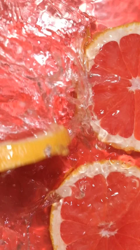 Juicy grapefruit slice dropping from above creating water splash, overhead view. Stock Footage 340550219