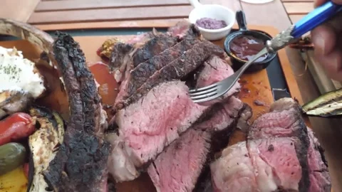 Juicy Grilled Tomahawk Steak Sliced on Wooden Board with Charred Vegetables and Stock Footage 338210744