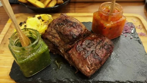 Juicy large freshly cooked beef steak on a wooden board with sauces and potatoes Stock Footage 304444937