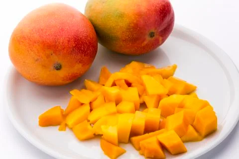 Juicy mango dice and two entire mangos on a plate Stock Photos