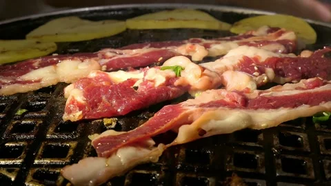 Juicy marinated beef slices sizzle on a Korean BBQ grill Vídeos de archivo 337214313