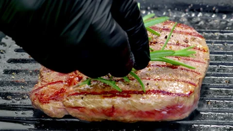 Juicy medium rare beef steak is cooked on a cast iron pan The chef adds rosemary Stock-Footage 315903176