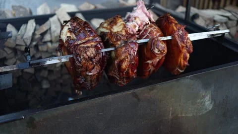 Juicy, perfectly roasted meat turning on a spit over a wood-fired grill. The gol Video stock 293469656