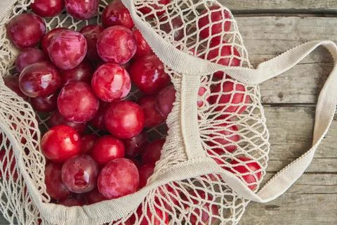 Juicy plums in eco friendly string eco mesh bag on a wooden background top view Stock Photos