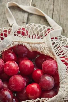 Juicy plums in eco friendly string eco mesh bag on a wooden background top view Stock Photos