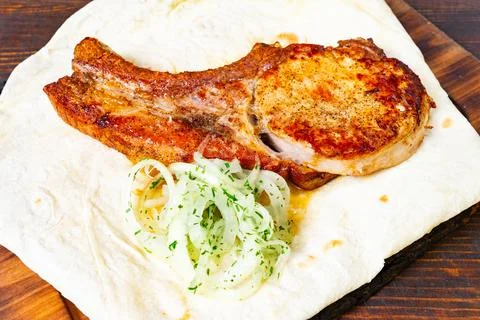 Juicy pork chop served on flatbread with onions and herbs Stock Photos