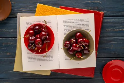 Juicy red sweet cherries with tails lying in two bowls on the pages of an open Stock Photos
