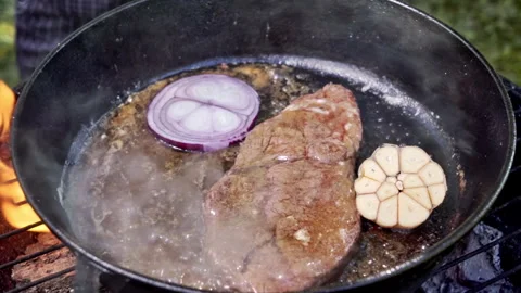Juicy steak is being cooked in a cast iron pan over coals and fire on the grill Stock Footage 315279870