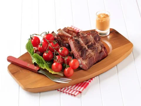 Juicy steak with cherry tomatoes and herbs on a board Stock Photos