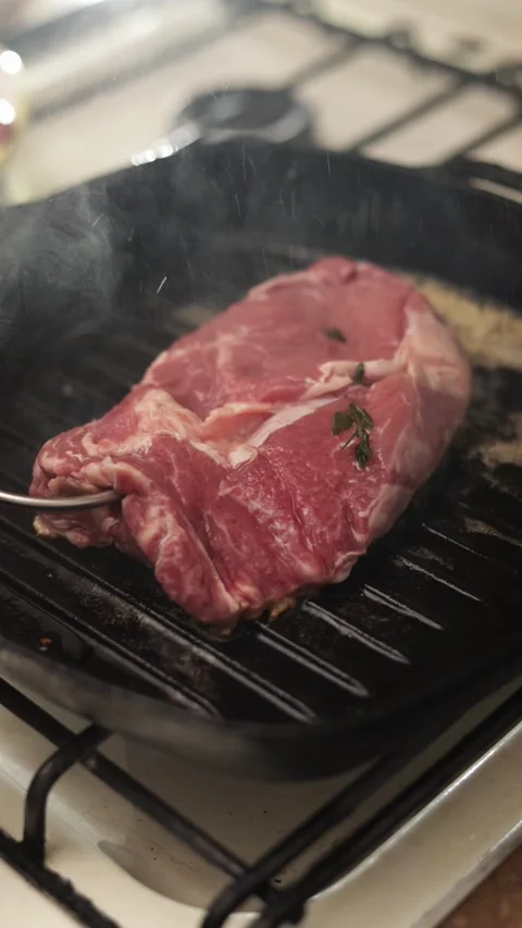 Juicy steak sizzling on a grill pan with fresh herbs and steam rising Stock Footage 340562864
