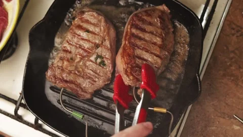 Juicy steaks searing in a hot cast iron grill pan with butter and herbs Stock Footage 340563324