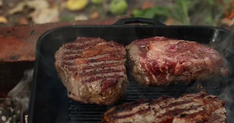 Juicy steaks sizzling on a cast iron grill pan with visible flames Stock Footage 339074232