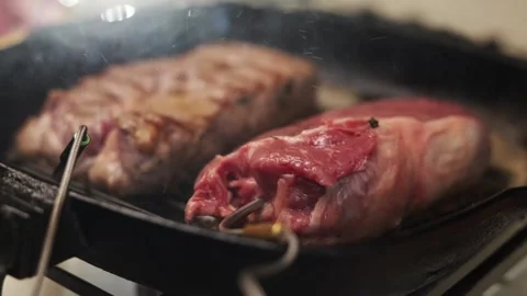 Juicy steaks sizzling in a cast iron grill pan with smoke rising Vidéo 340563322