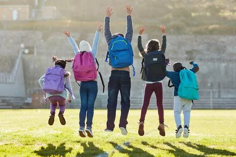 Jumping for joy. Rearview shot of elementary school kids jumping outside. Stock Photos