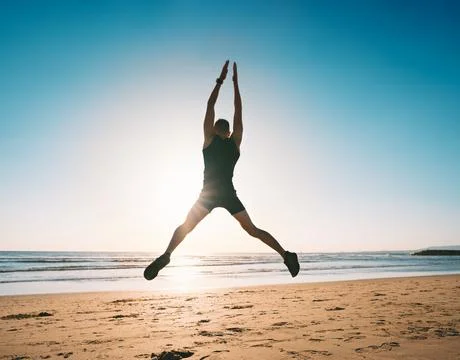 Jumping man. Young man doing jumping jacks or star jump exercise on the beach Stock Photos